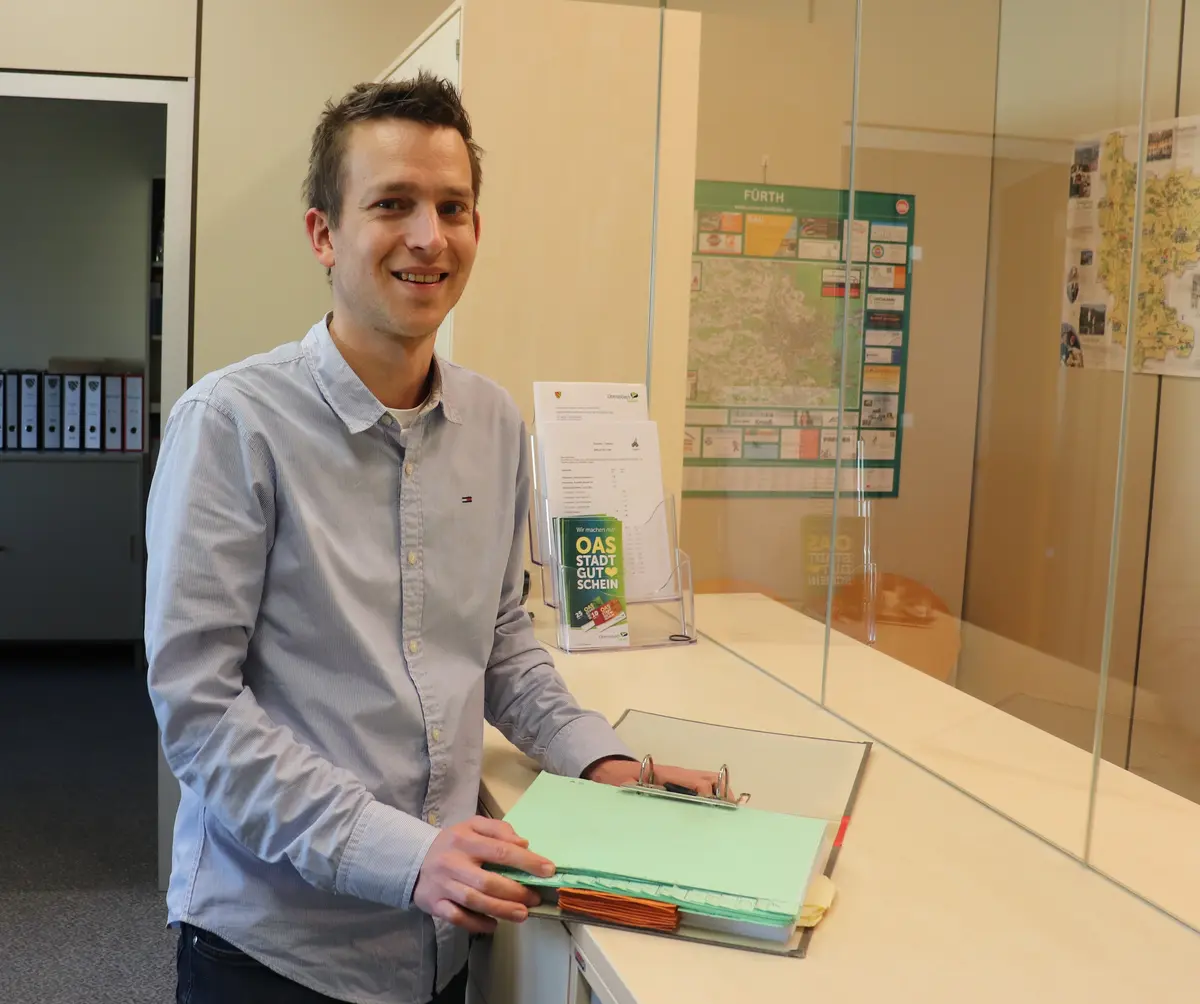 Christian Kuhn steht mit einem Dokumentenordner am Kassentresen. 