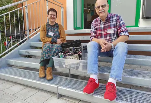 Eine Frau und ein älterer Herr sitzen auf den Stufen vor dem Oberasbacher Jugendhaus, zwischen sich ein kaputter Kaffeevollautomat.