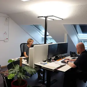 Zwei Personen arbeiten an ihren gegenüberliegenden Schreibtischen im Büro