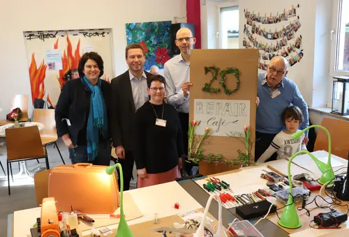 Bürgermeisterin Birgit Huber, Landrat Matthias Dießl und der Vorstand der Diakonie Fürth, Stephan Butt, stehen gemeinsam mit Quartiersmanagerin Renate Schwarz und dem Initiator Dietmar Fechner um eine Schild 20. Repai-Café