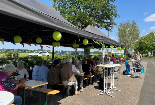 Zahlreiche Menschen sitzen im Pavillion an Biertischen und tauschen sich aus.