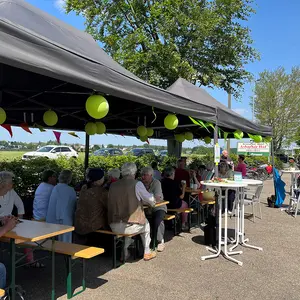 Zahlreiche Menschen sitzen im Pavillion an Biertischen und tauschen sich aus.