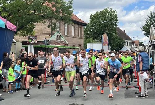 Junger Männer mit Trikots und Startnummern laufen durch einen Altstadtort. 