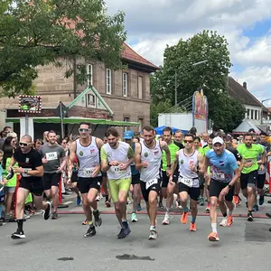 Junger Männer mit Trikots und Startnummern laufen durch einen Altstadtort. 
