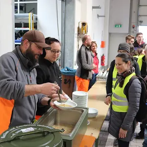 Ein Mann und eine Frau geben Essen an die in der Schlange wartenden Menschen aus.