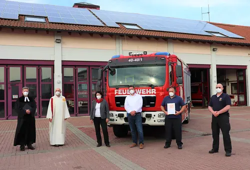 Vor dem Feuerwehrgerätehaus und dem neuen Löschfahrzeug haben sich sechs Personen zum Foto mit Abstand aufgestellt