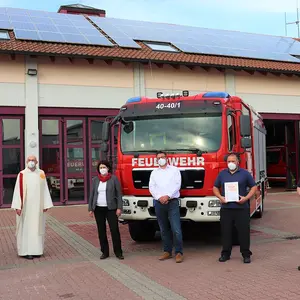 Vor dem Feuerwehrgerätehaus und dem neuen Löschfahrzeug haben sich sechs Personen zum Foto mit Abstand aufgestellt