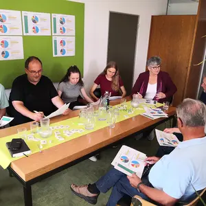 Acht Personen sitzen um den Tisch und begutachten die Unterlagen.