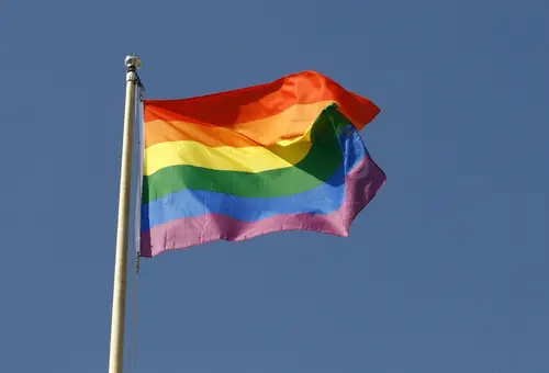 Flaggenamst mit Regenbogenflagge in den Farben rot - orange - gelb - grün - blau - lila (von oben nach unten)