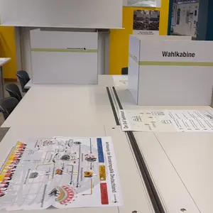 Blick auf zwei Wahlkabinen. Davor auf einem Tisch findet man noch Informationen zum Wahlsystem.