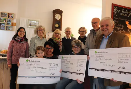 Sechs Frauen, drei Männer und ein Kind halten drei große symbolische Schecks bei der Spendenübergabe. 