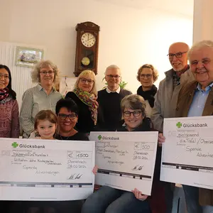 Sechs Frauen, drei Männer und ein Kind halten drei große symbolische Schecks bei der Spendenübergabe. 