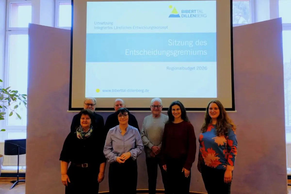 Sieben Männer und Frauen vor einer Wand mit einer Präsentation