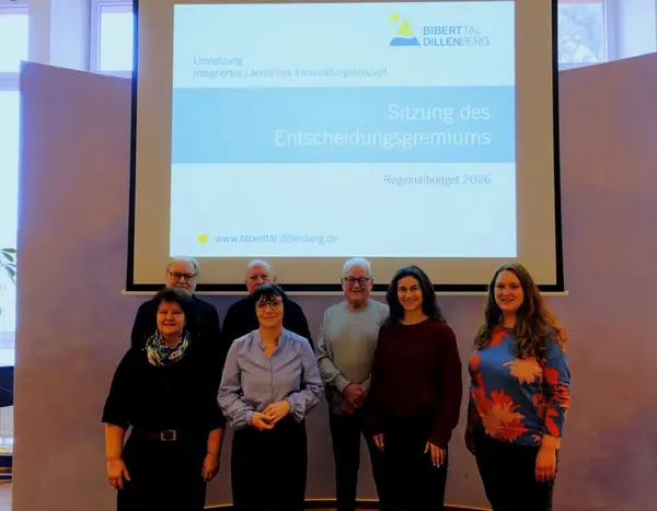 Sieben Männer und Frauen vor einer Wand mit einer Präsentation