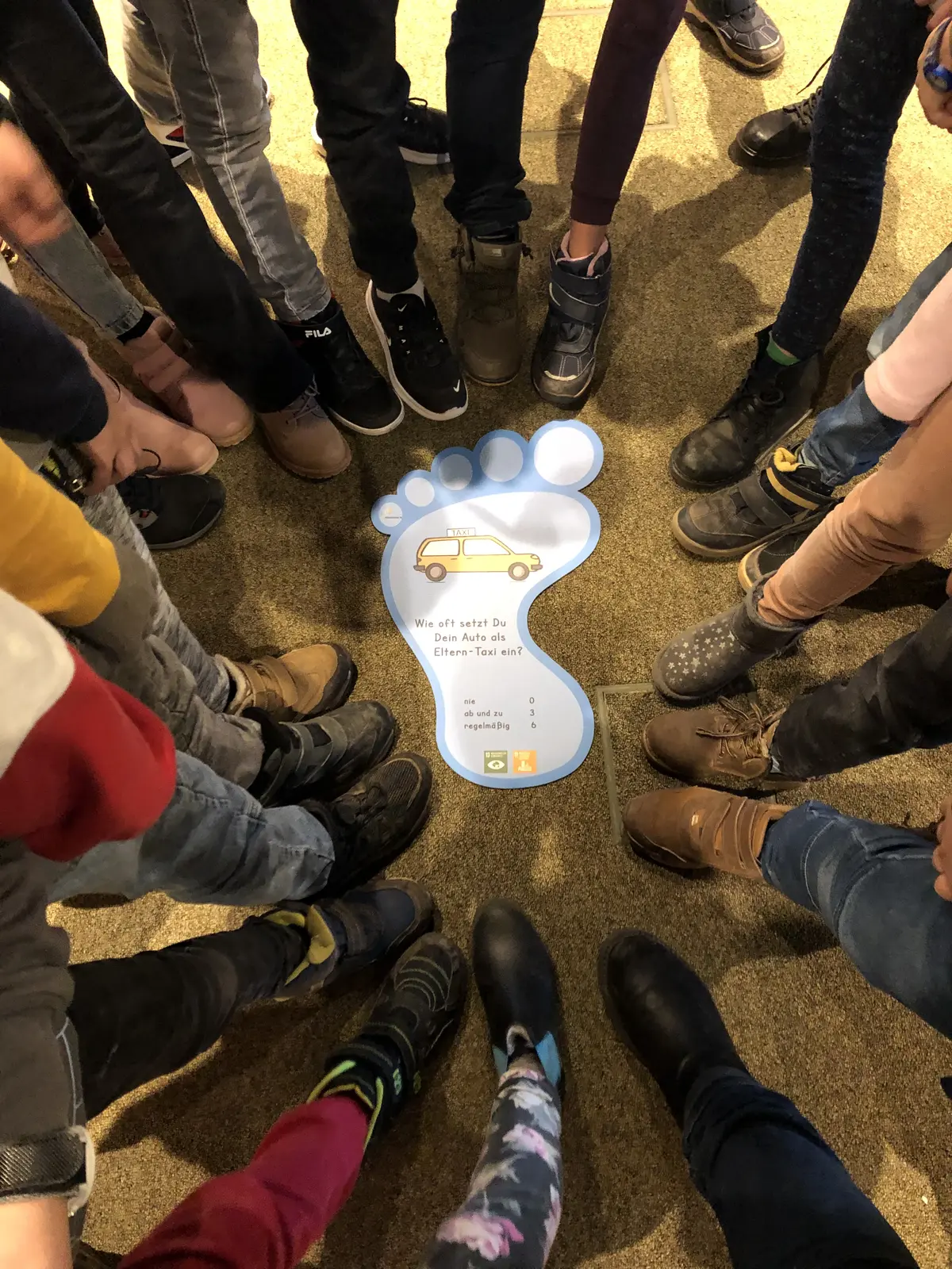 Ein Kreis aus Füßen, in der Mitte ein Fuß aus Pappe mit der Statistik "Wie oft setzt du dein Auto als Elterntaxi ein?" Nie null Stimmen, ab und zu drei Stimmen, regelmäßig 6 Stimmen. 