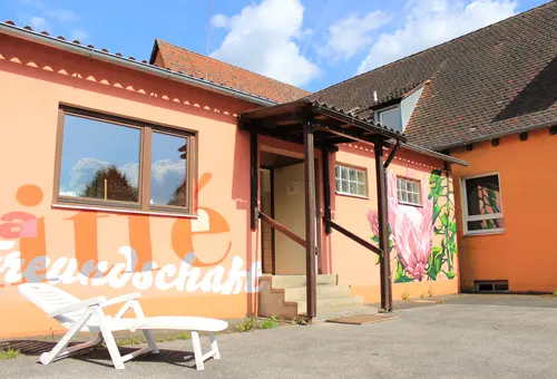 Innenhof des Jugendhauses OASIS; weiße Sommerliege vor orange gestrichener Wand 