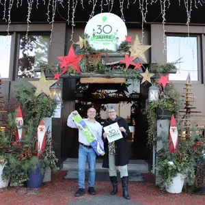 M. Träger und B. Huber vor dem Eingang des Rathauses. Träger hält Programm in der Hand, Huber das Jubiläumslogo