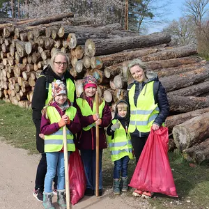 Zwei Mütter mit drei Kindern vor einem Holzstapel.
