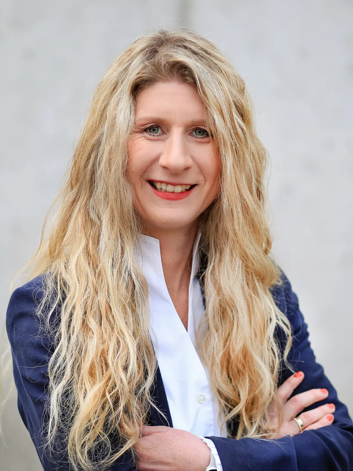 Frau mit langen blonden Locken, weißer Bluse und blauer Anzugjacke