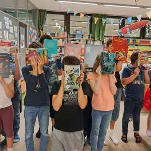 Eine Gruppe von Kindern hält Bücher vor ihre Gesichter. 