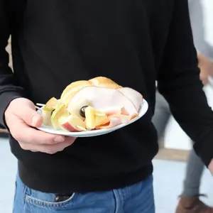 Eine Hand hält einen Teller mit Obst, Brötchen und Putenwurst