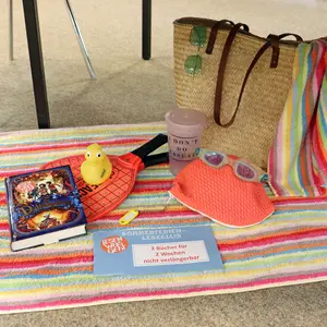 Eine Picknickdecke mit Strohtasche, Strandutensilien und Büchern. 