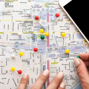 Zwei Hände stecken Nadeln in einen Stadtplan, daneben liegt ein Taschenrechner.