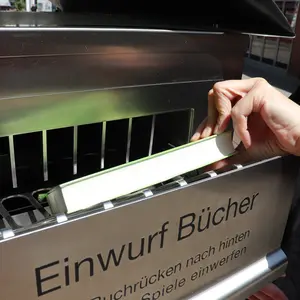 Hand, die ein Buch in die Schublade "Einwurf Bücher" steckt. 