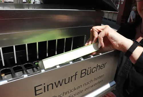 Hand, die ein Buch in die Schublade "Einwurf Bücher" steckt.