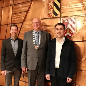 Drei Herren vor der mit Kupfer beschlagenen Wand des Sitzungssaals