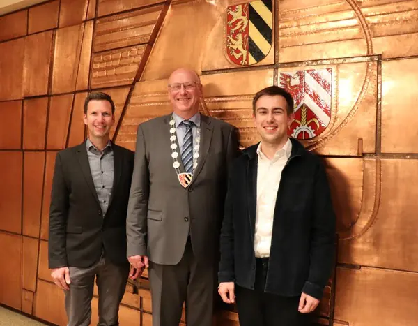 Drei Herren vor der mit Kupfer beschlagenen Wand des Sitzungssaals