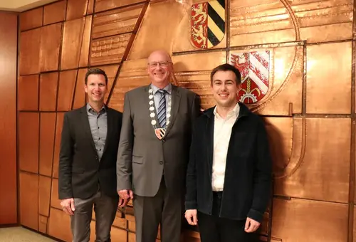 Drei Herren vor der mit Kupfer beschlagenen Wand des Sitzungssaals