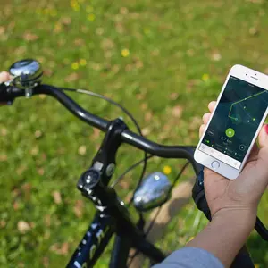 Blick von oben auf einen Fahrradlenker. Das Fahrrad steht auf einer grünen Wiese. Der/die Lenkende hält ein Handy mit der Stadtradeln-App in der Hand. hält in der rechten 