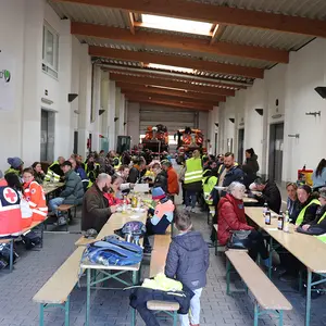 Blick in die Fahrzeughalle des Bauhofs mit Menschen an den Bierbänken.