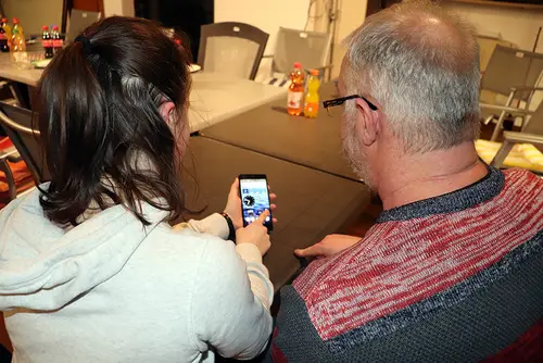 Eine Jugendliche zeigt einem Herrn die Funktionen des Mobiltelefons.