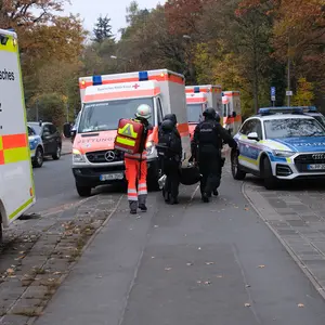 mehrere Polzei- und Rettungswagen mit Personen davor