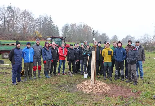 Gruppe von Schülern und Verantwortlichen mit jungem Baum im Vordergrund 