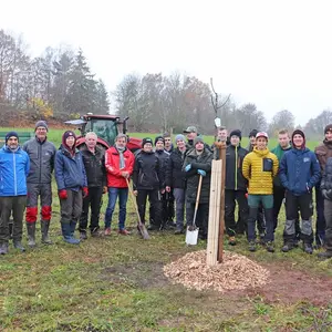 Gruppe von Schülern und Verantwortlichen mit jungem Baum im Vordergrund 