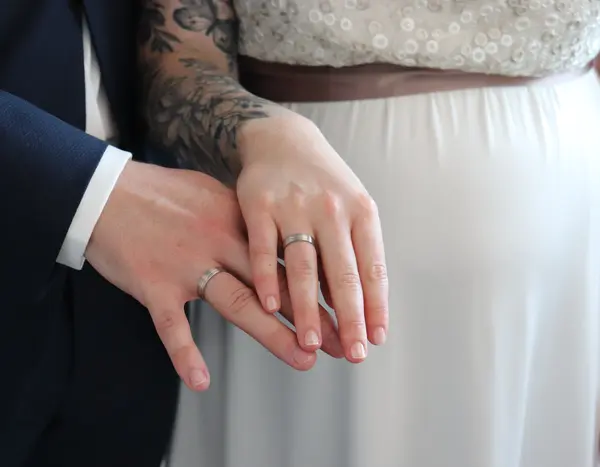 Die Hand des Bräutgams und die Hand der Braut jeweils mit dem Ehering.