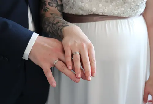 Die Hand des Bräutgams und die Hand der Braut jeweils mit dem Ehering.