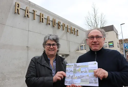 Eine Frau und ein Mann präsentieren vor der Rathausplatzmauer das neue Stadtentwicklungskonzept