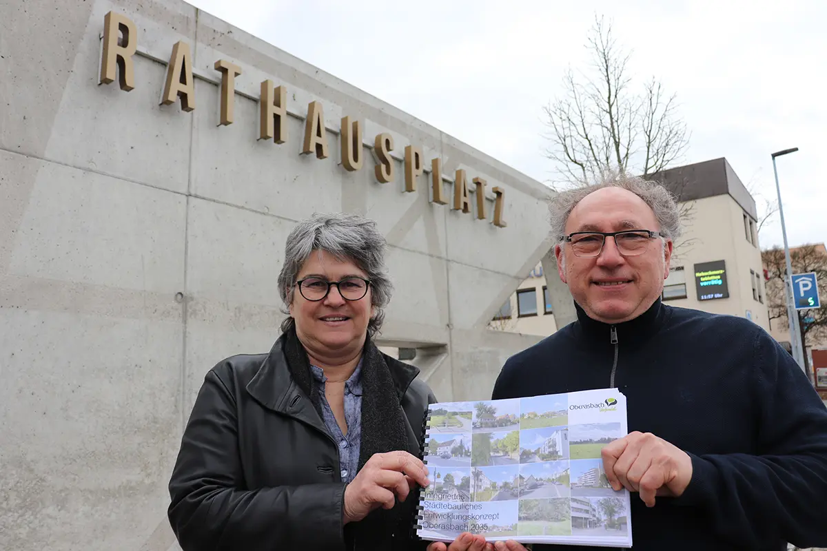 Eine Frau und ein Mann präsentieren vor der Rathausplatzmauer das neue Stadtentwicklungskonzept