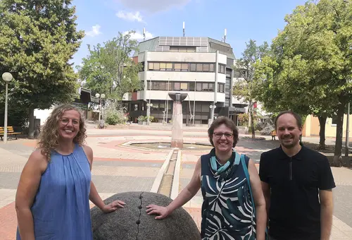 Zwei Frauen und ein Mann an der großen Steinkugel am Brunnen auf dem Rathausplatz. Im Hintergrund das Rathaus.