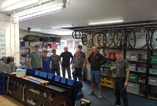Acht Männer stehen in einer Fahrradwerkstatt
