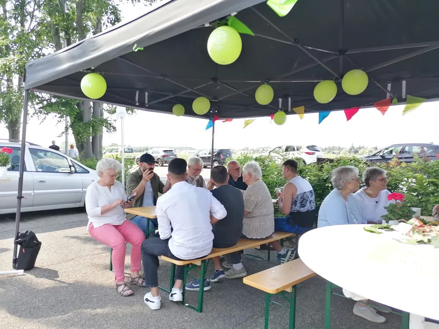 Menschen auf Bierzeltgarnituren unter Pavillons mit Luftballons auf einem Parkplatz