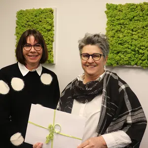 Zwei Frau halten einen Geschenkumschlag vor sich.