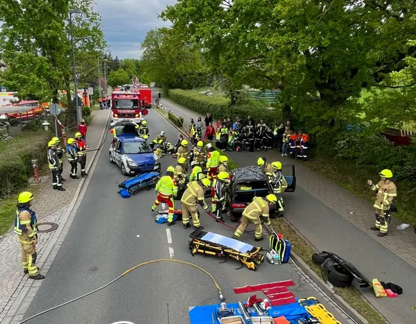 Straße mit mehreren Einsatzfahrzeugen, einer Trage für Verletzte und Feuerwehrpersonen in Schutzkleidung