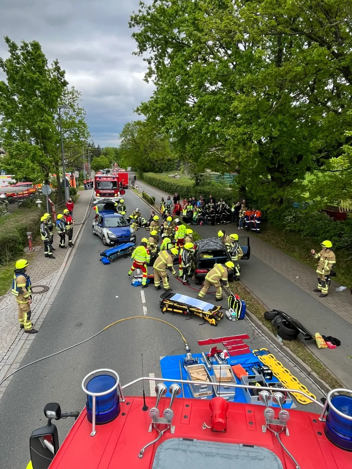 Straße mit mehreren Einsatzfahrzeugen, einer Trage für Verletzte und Feuerwehrpersonen in Schutzkleidung