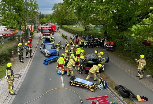 Straße mit mehreren Einsatzfahrzeugen, einer Trage für Verletzte und Feuerwehrpersonen in Schutzkleidung