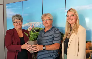 Eine Frau überreicht einem Mann eine Topfpflanze, rechts daneben steht eine junge Frau